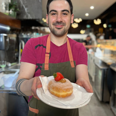 Best-restaurants-downtown-edmonton-donut-decorating-for-international-donut-day-on-a-donut-bike-tour-on-international-donut-day-Edmonton-best-bakers-Edmonton-Alessandro-from-Ayco-Cafe-holding-plate-with-a-donut-topped-with-a-strawberry-food-bike-tour